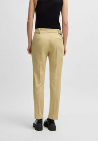 Jasnożółte spodnie woskowane, o dopasowanym kroju, z gładką fakturą, tylną kieszenią i noszone z czarnymi butami.
