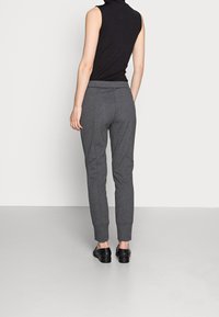 Grijze, taps toelopende sweatpants met een elastische tailleband en boorden aan de enkels, gemaakt van een zacht materiaal; gedragen met een mouwloos zwart topje.