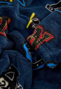 Fleece tæppe i marineblå, med farverige geometriske mønstre og teksturer. Blødt, fluffy materiale med livlige accenter i rød, gul og blå.