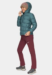 Turkusowa kurtka puchowa z kapturem, dopasowany krój i pikowana faktura. W komplecie z bordowymi spodniami i szarymi butami wędrownymi. Włóczkowa czapka dopełnia stylizację.