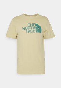 Camiseta de algodón color amarillo claro con un logotipo gráfico verde "THE NORTH FACE" y un elemento de diseño curvado en la parte frontal. Mangas cortas.