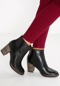 Bottines en cuir noir avec une finition texturée, fermeture éclair sur le côté et motif perforé, dotées d'un talon en bois empilé.