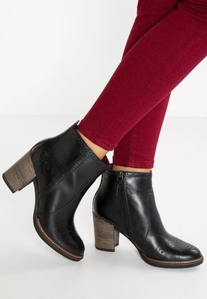 Bottines en cuir noir avec une finition texturée, fermeture éclair sur le côté et motif perforé, dotées d'un talon en bois empilé.