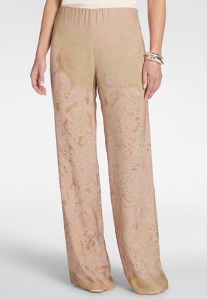 Pantalon beige à jambes larges avec motif paisley rose subtil, porté avec un haut blanc et des bracelets argentés au poignet droit.