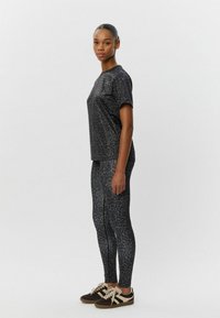 Čierny športový set s leopardím vzorom, ktorý obsahuje tričko s krátkym rukávom a legíny, doplnený tmavými teniskami, zdôrazňujúci hladkú a elastickú látku.