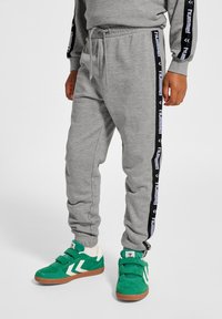 Grå sweatpants med svarta sidostråck som har "hummel"-loggan, elastisk midja och avslappnad passform. Matchat med gröna och vita sneakers med kardborre. 