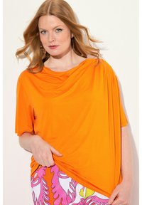 Přetáhnutý oranžový top s volným výstřihem a krátkými rukávy, spárovaný s růžovými a bílými vzorovanými kalhotami. Měkká, hladká látka.