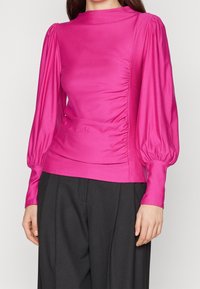 Välskräddad rosa blus med långa puffärmar och rynkdetaljer på sidan, tillverkad av ett slätt, glänsande tyg.