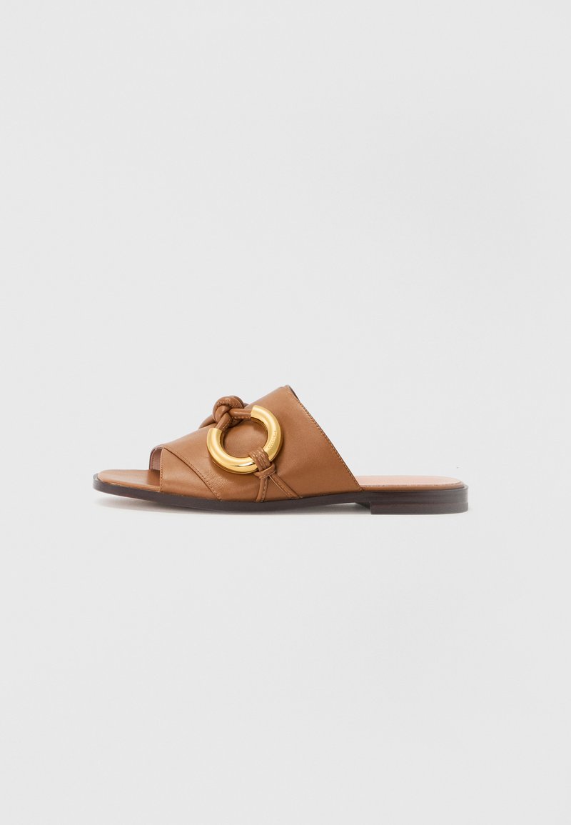 Brune lærerslide sandaler med en knyttet stropp og en stor gullsirkel aksent. Flat såle med minimalistisk design. Åpen tå stil.