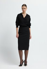 Schwarze, langärmlige Button-up-Bluse mit einem dezenten Leopardenmuster, kombiniert mit einem figurschmeichelnden schwarzen Bleistiftrock und schwarzen hochhackigen Schuhen.