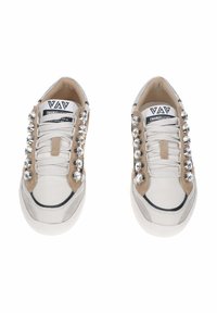 Sneakers bianchi in pelle con dettagli in camoscio beige, borchie argentate lungo i lati, finiture nere e lacci bianchi. Presenta un logo stampato sulla linguetta.