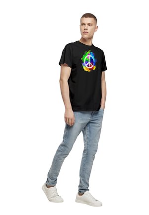 Svart bomull T-skjorte med et fargerikt fredssymboldesign med sprut av rødt, oransje, gult, grønt, blått og lilla. Blå jeans og hvite joggesko.