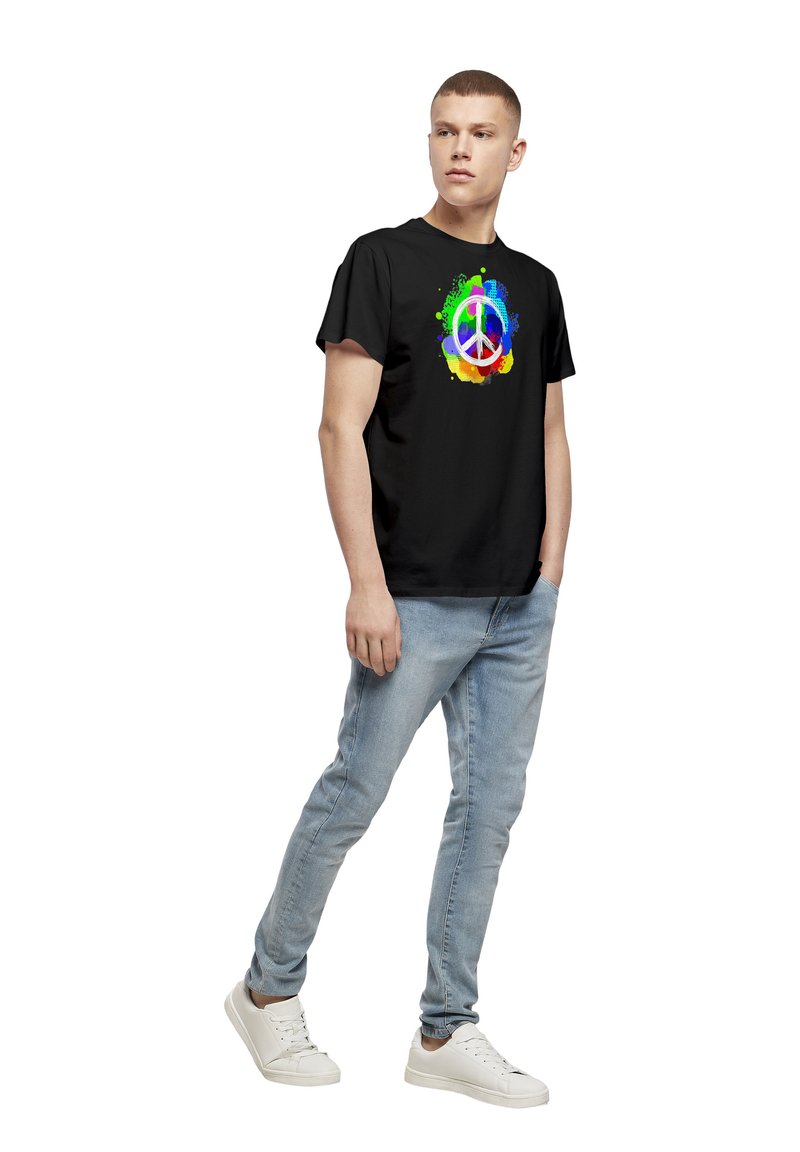 Svart bomull T-skjorte med et fargerikt fredssymboldesign med sprut av rødt, oransje, gult, grønt, blått og lilla. Blå jeans og hvite joggesko.