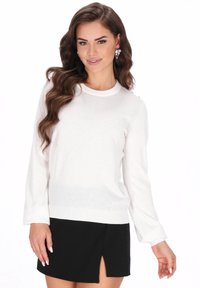 Witte trui met lange mouwen, ronde hals en geribbelde zoom, gecombineerd met een zwarte minirok met een zijsplit. Overal een gladde textuur.