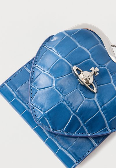 Μπλε πορτοφόλι σε σχήμα καρδιάς από συνθετικό δέρμα κροκοδείλου με ασημένιο έμβλημα δαχτυλιδιού πλανητών σε λευκό φόντο.