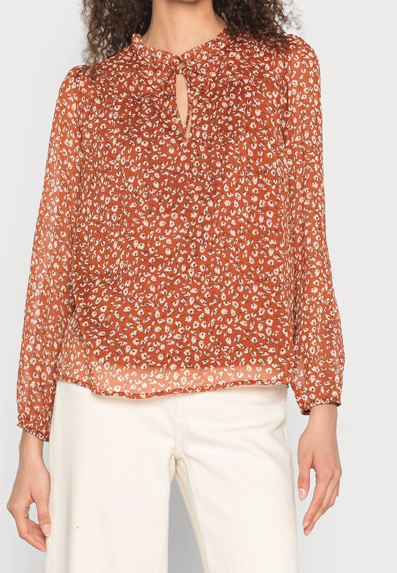 Rustfarbene Bluse mit Floralprint, Schlüssel-Ausschnitt und langen Ärmeln. Hergestellt aus leichtem, transparentem Material, das eine lockere Passform bietet.