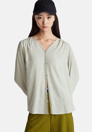 Crème gestreepte blouse met een V-hals, lange mouwen en een relaxed fit, gecombineerd met olijfgroene broeken. Pet met een zwart logo.