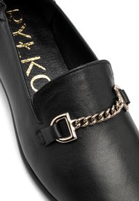Czarna skórzana sznurowana odzież z okrągłym noskiem, zdobiona metalowym łańcuchem i detalem z klamrą. Teksturowane wnętrze i płaska podeszwa.
