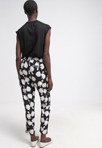 Schwarzes ärmelloses Top, gemusterte Hosen im schwarz-weißen Blumenmuster, elastischer Bund, taillierter Schnitt und knöchellang mit Seitenschlitzen.
