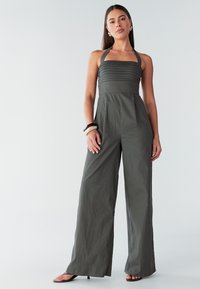 Donkergrijze jumpsuit met een aangesloten, geplooide bovenkant, brede pijpen en halterbandjes. Soepele textuur en minimale naden; geen patronen of hardware.