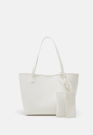 Biała torba na ramię z miękkiej skóry z dwoma długimi uchwytami oraz małą dopasowaną saszetką na zatrzask w kolorze złotym na jednolitym tle.