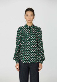 Chemise verte à boutons avec un motif géométrique en rose et vert foncé. Manches longues, coupe décontractée et design de col classique.