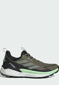 Zapato de senderismo GORE-TEX con una parte superior sintética verde y negra, que presenta una textura de malla, una entresuela blanca acolchada y una suela exterior negra y resistente.