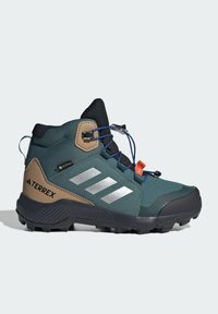 Grønne og svarte mid-cut tursko med teksturert overdel, sølvfargede detaljer, GORE-TEX-merke og en robust såle med markerte mønster.
