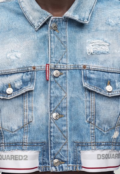 Φωτεινό γαλάζιο φθαρμένο τζιν μπουφάν με μεταλλικά κουμπιά, τσέπες με καπάκια στο στήθος και κόκκινη ετικέτα "DSQUARED2" στο μπροστινό ύφασμα.