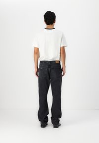 Black denim jeans with a straight fit, featuring back pockets and a leather patch at the waist. Paired with a white T-shirt.