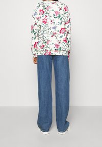 Sudadera de manga larga con estampado floral en color crema, combinada con vaqueros de corte holgado en azul. Presenta puños y cinturilla elásticos, con una silueta relajada.