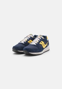 Navy blue sneakers with yellow accents, suede and mesh materials, padded collar, and white laces. Features a black rubber outsole.