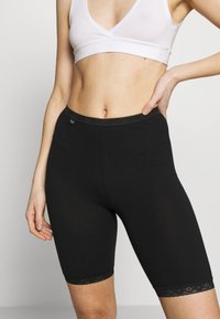 Pantaloni ciclisti neri realizzati in un morbido tessuto elasticizzato. Presentano un bordo in pizzo all'orlo e una vita elastica per una vestibilità comoda.