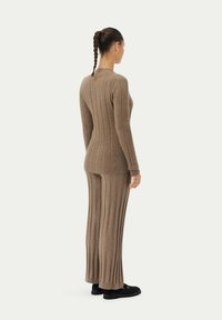 Brun ribbad stickad tröja och matchande byxor, med vertikala linjer, tajt passform och en mjuk textur. Stylad med svarta skor.