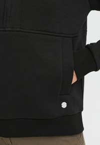 Felpa nera con finitura testurizzata, polsini e orlo a costine. Dotata di una tasca laterale e di un logo circolare in argento vicino alla vita.