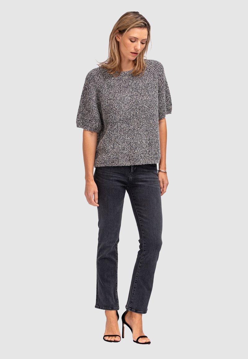 Pull gris à manches courtes avec un tricot texturé, associé à un jean foncé et des talons noirs à lanières, créant un look à la fois décontracté et soigné.