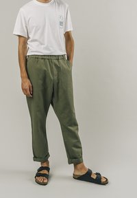 Bílá bavlněná tričko s grafickým potiskem, olivově zelené elastické kalhoty v pase, černé sandály s korkovou stélkou a ohrnuté manžety.