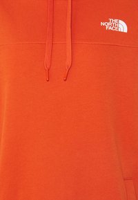 Sweat à capuche orange avec cordons de serrage et logo blanc "The North Face" sur la poitrine.