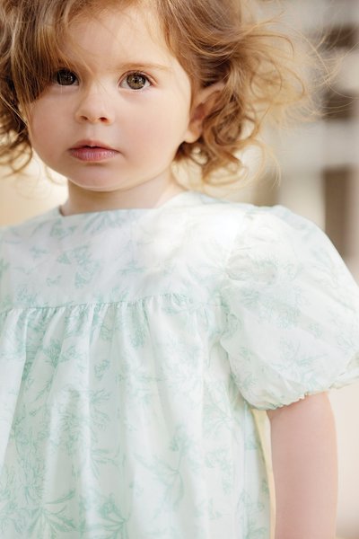 Lys grøn blomsterkjole med puffærmer, med en samlet bodice. Blødt, letvægtsmateriale med et delikat mønster velegnet til børn.
