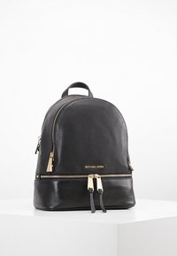 Sac à dos en cuir noir de forme arrondie, avec des accessoires en or, deux compartiments zippés et une poignée supérieure pour le transport.