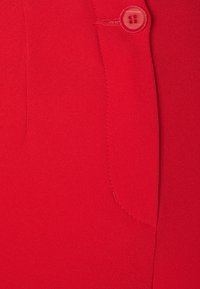 Tissu rouge avec une texture lisse, comportant une poche et un bouton rond transparent près du haut. Design simple avec des lignes épurées.