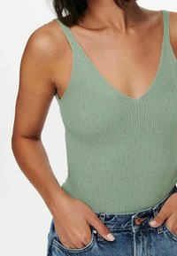 Bodysuit vert côtelé avec un décolleté en V profond et de fines bretelles, présentant une texture douce. Associé à un short en denim taille haute.