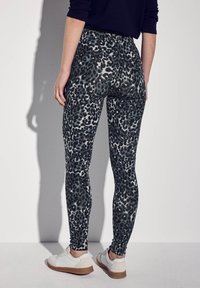 Panterprint leggings van rekbare stof, met een hoge tailleband en een gladde textuur, gecombineerd met witte sneakers en bruine zolen.