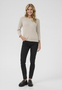 Maglione beige a coste con scollatura rotonda, maniche a tre quarti, indossato con pantaloni neri slim-fit e mocassini neri con piattaforma.