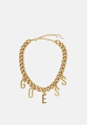 Gouden ketting met grote schakels en hangers in de vorm van letters die "GUESS" spellen, voorzien van een verstelbare sluiting met een rhinestone-accent.