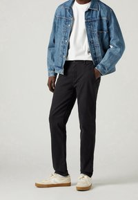 Giacca di denim blu chiaro con chiusura a bottoni, t-shirt bianca a collo rotondo, pantaloni neri e sneakers color crema con dettagli bianchi e beige.