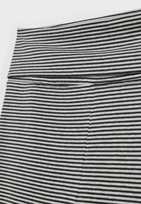 Schwarz-weiß gestreifter Stoff mit glatter Textur, ausgestattet mit einem gefalteten Bund und sichtbaren Nahtdetails.