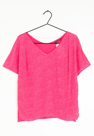 Blusa rosa a maniche corte con scollatura a V, realizzata in un tessuto leggero con un motivo testurizzato di piccoli pois bianchi. L'orlo presenta una leggera curvatura.