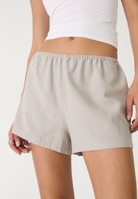 Pantalones cortos de algodón tejido de color gris claro con una cintura elástica. Presentan un corte relajado y un diseño simple y sin adornos.