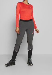 Dlouhý rukáv, jasně červený top spojený s přiléhavými šedými legínami s růžovými a černými akcenty, vyrobenými z pružného materiálu odvádějícího vlhkost.